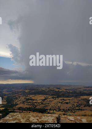 Sturmfront auf den sanften Hügeln: Ein Zusammenprall zwischen den Kräften der Natur. Dunkler Himmel über der sonnendurchfluteten Landschaft: Ein dramatischer Klimawandel. Kontrast Stockfoto