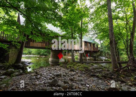 Pittman Center, Tennessee, USA, 20. Juli 2024: Blick auf die überdachte Emerts Cove Bridge vom Little Pigeon River Ufer aus. Stockfoto