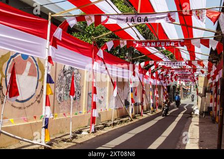 Bandung Regency, West Java, Indonesien. August 2024. Ein Motorradfahrer passiert eine Straße mit rot-weißen Verzierungen, die den 79. Unabhängigkeitstag der Republik Indonesien begrüßt, und 70 Meter rotes und weißes Tuch schmücken Cileunyi Kulon Village, Bandung Regency, West Java. (Kreditbild: © Dimas Rachmatsyah/Pacific Press via ZUMA Press Wire) NUR REDAKTIONELLE VERWENDUNG! Nicht für kommerzielle ZWECKE! Stockfoto