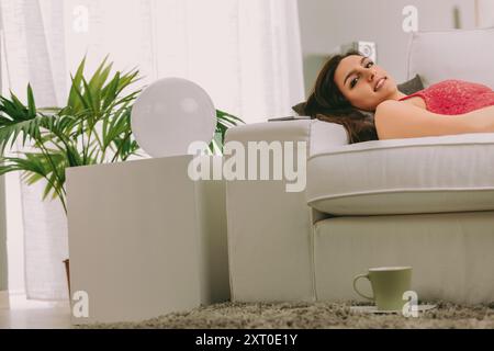 Die Frau liegt bequem auf einer Couch und nimmt ihren Urlaub einfach durch Ausruhen an. Im Gegensatz zu anderen, die gerne auf Entdeckungsreise sind, entschließt sie sich, ihre Freizeit zu genießen und zu genießen Stockfoto