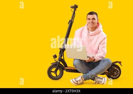 Junger Mann mit Elektroroller mit Laptop auf gelbem Hintergrund Stockfoto