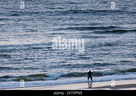 Silhouette eines Fischers, der bei Sonnenaufgang am Strand vor dem Meer steht Stockfoto