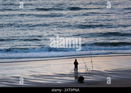 Silhouette eines Fischers, der bei Sonnenaufgang am Strand vor dem Meer steht Stockfoto