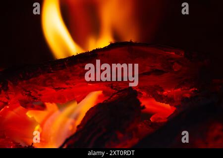 Helle orange Flammen um brennendes Holz im Dunkeln, Nahaufnahme Stockfoto