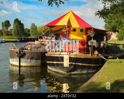 Abingdon behauptet, die älteste Stadt Englands zu sein. Und die Themse verläuft durch das Herz. Hier sehen wir zwei farbenfrohe Lastkähne, die an den Feldern der Abtei vertäut sind, mit Utensilien und Zelten für einen Jahrmarkt, der auf der anderen Seite des Flusses errichtet wird. Stockfoto