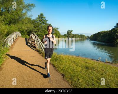 Dies ist ein Teil des Thames Path - und Flusses - zwischen den Iffley Locks und den Bootshäusern der Oxford University von Christ Church Meadows. Es wird oft von Ruderern, Wanderer, Joggern, Radfahrern und Hundeschlitten - und sogar von Fotografen besucht. Sehr früh an einem schönen Mittsommertag, aber nur dieser einsame Jogger hat es geschafft. Und natürlich auch mich. Stockfoto