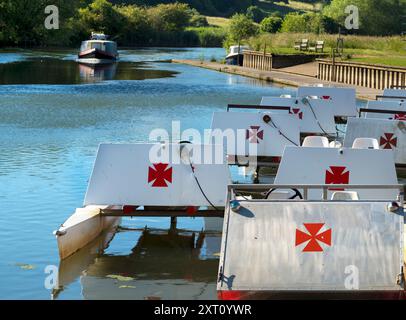 Das 1921 gegründete Radley Boathouse befindet sich an einem wunderschönen Teil der Themse in Oxfordshire und dient seit über einem Jahrhundert Radley College und lokalen Ruderfreunden. Hier sehen wir eine Reihe von Freizeitbooten, die an der Anlegestelle vor Anker liegen, während die Sonne aufgeht. Und ein Hausboot fährt vorbei... Warum das maltesische Kreuz? Das ist eine lange Geschichte... Diese wurde ursprünglich vom College als Abzeichen für alle Sportarten um 1850 angenommen. Es wurde zum Symbol des Boat Club von der frühesten bekannten Besatzung und wurde wahrscheinlich zu Ehren von Sir George Bowyer, dem Besitzer von Radley Hall, adoptiert, von dem das Haus und der Gr stammen Stockfoto