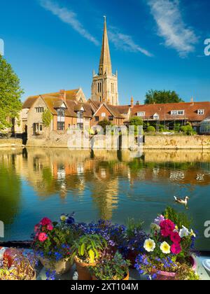 Eine schöne Aussicht auf die Themse in Abingdon, früh an einem Sommermorgen. Wir befinden uns am Südufer des Flusses und blicken über die angelsächsische Kirche St. Helens, nach der der Kai benannt ist, vorbei an einem mit Blumen bedeckten Hausboot im Vordergrund. Stockfoto