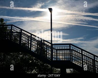 Selbst das Alltägliche kann zur richtigen Zeit und am richtigen Ort durch Schönheit verwandelt werden. Hier sehen wir die sich abzeichnende Brücke über die Gleise an einem verlassenen Radley Village Railway Station, mit einer Straßenlaterne, die vor einer leuchtenden Wolkenlandschaft und Dampfpfaden steht Stockfoto