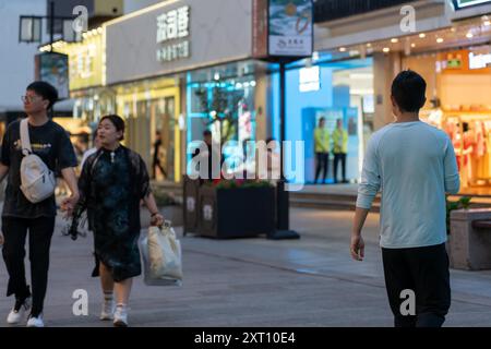 Suzhou, China - 11. Juni 2024 : Menschen laufen auf einem Bürgersteig vor Geschäften und Geschäften in einer Stadt. Stockfoto