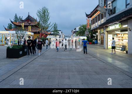 Suzhou, China - 11. Juni 2024 : Eine breite, gepflasterte Straße mit Geschäften und Gebäuden in Suzhou, China. Die Leute laufen die Straße entlang und genießen den Abend Stockfoto
