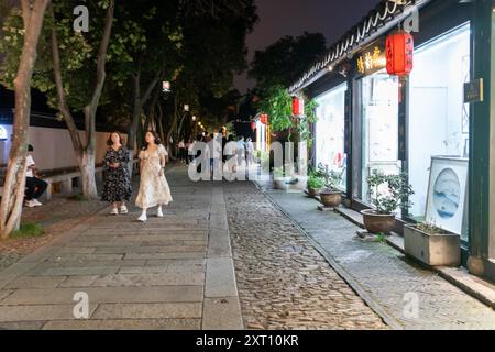 Suzhou, China - 11. Juni 2024 : Eine enge Kopfsteinpflasterstraße in Suzhou, China, gesäumt von traditionellen Läden und Laternen. Stockfoto