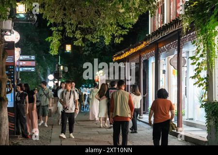 Suzhou, China - 11. Juni 2024 : nächtliche Straßenszene in Suzhou, China, mit Menschen, die an traditionellen Geschäften und Gebäuden vorbeilaufen. Stockfoto