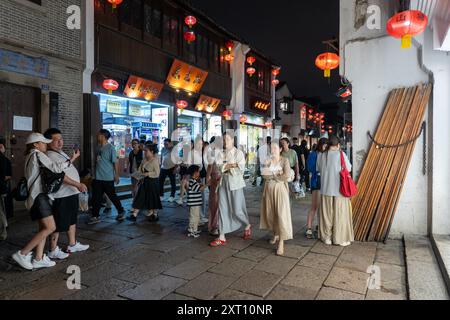 Suzhou, China - 11. Juni 2024 : Eine nächtliche Straßenszene in Suzhou, China, mit roten Laternen, die über einer Menschenmenge hängen, die auf einem Kopfsteinpflaster läuft Stockfoto