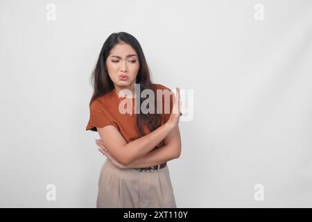 Verärgerte junge asiatische Frau, die braunes Hemd trägt, das Stoppschild mit der Handfläche über weißem isoliertem Hintergrund macht. Stockfoto