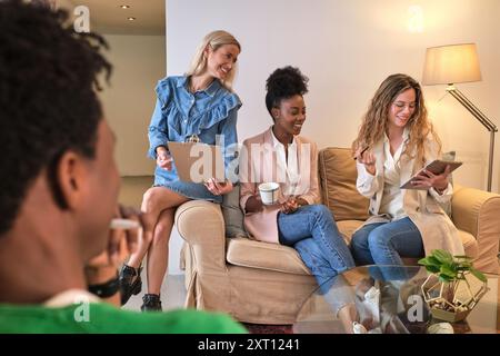 Gesellschaft von verschiedenen Mitarbeitern, die sich auf dem Sofa in der Bürolounge treffen und gemeinsam Geschäftsprojekt diskutieren Stockfoto