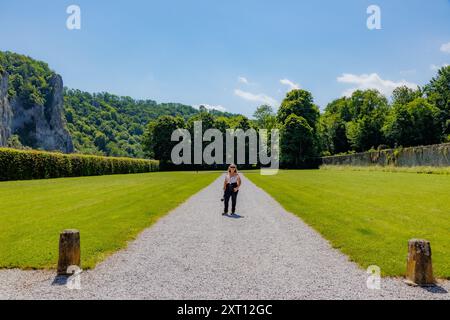 Schotterweg mit weiblichen Touristen, die im Garten vor Freyr Castle stehen, üppige Bäume und felsige Berge vor blauem Himmel vor verschwommenem Hintergrund, sonnige s Stockfoto