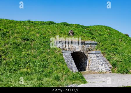 Unterirdischer Tunnel, der zu einem der Komplexe der Festung Charlemont führt, grünes Gras auf einem Hügel vor blauem Himmel, dicke Steinmauern und bogenförmiger Eingang, su Stockfoto