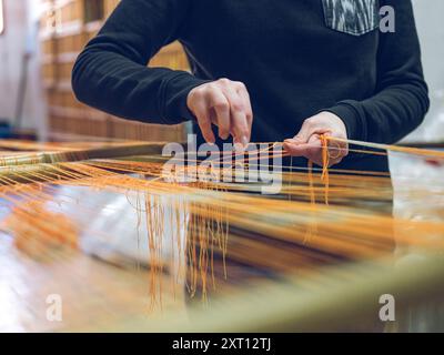 Nahaufnahme von Händen, die Garn auf einem Webstuhl in einer traditionellen Textilfabrik mit einem anonymen Arbeiter manuell weben Stockfoto