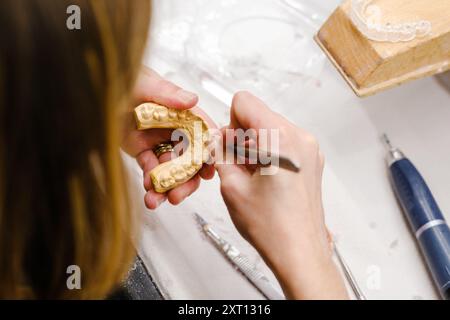 Von oben hält ein nicht wiedererkennbarer Zahntechniker einen goldenen Zahnabdruck, während er im Labor daran arbeitet und dabei Präzision und e zeigt Stockfoto