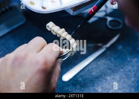 Von oben abgeschnittene, nicht erkennbare Nahaufnahme der Präzisionsarbeit eines Zahntechnikers an einer Prothese mit Hilfe eines Werkzeugs. Stockfoto