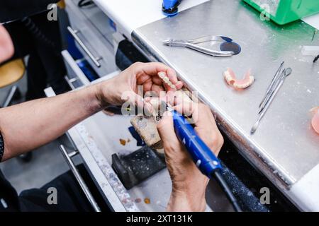 Von oben abgeschnittene, nicht erkennbare Nahaufnahmen der Hände eines Zahntechnikers bei der Arbeit an Prothesen mit Präzisionswerkzeugen im Labor. Stockfoto