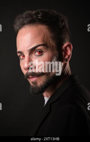 Ein mysteriöser Mann mit intensiv roten Augen und einem Spitzbart, der mit roten Kontaktlinsen durchdringend in die Kamera schaut Stockfoto