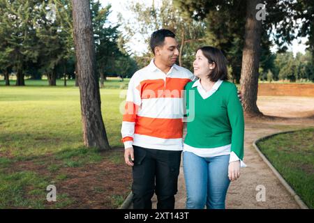 Liebevolles junges Latino-Paar, das gemeinsam in einem üppigen grünen Park spaziert und einen Moment der Zweisamkeit und Verbindung teilt Stockfoto
