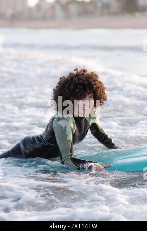 Seitenansicht einer jungen, glücklichen Surferin im Neoprenanzug, die auf dem wehenden Meerwasser liegt und den Sommertag genießt Stockfoto