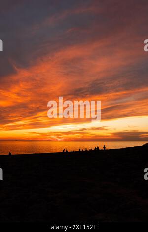 Spektakuläre Aussicht auf Reisende Silhouetten betrachten Meer vom Strand unter bunten bewölkten Himmel bei Sonnenuntergang Stockfoto