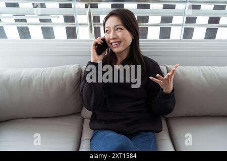 Eine freudige Frau führt ein angenehmes Gespräch auf ihrem Handy, während sie bequem auf einer Couch sitzt Stockfoto