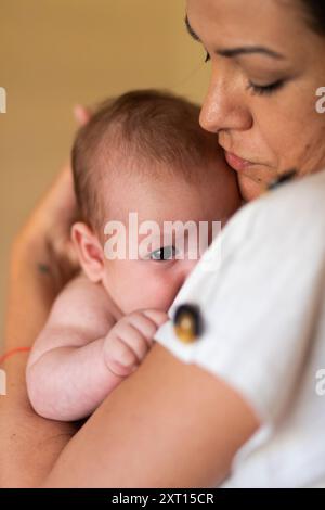 Seitenansicht der Ernte ruhige junge Frau umarmt und streichelt entzückendes Baby am Tag Stockfoto