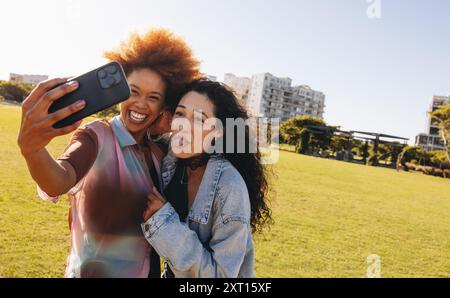 Zwei Teenager machen ein verspieltes Selfie im Freien, einer macht ein albernes Gesicht, indem er ihre Zunge rausstreckt. Stockfoto