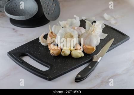 Knoblauch auf Schneidebrett Nahaufnahme. Ganze und gebrochene Knoblauchköpfe, geschälte und ungeschälte Zehen auf PP-Schneidebrett, Schwerpunkt auf Details, hohe Auflösung. Stockfoto