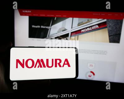 Person mit Smartphone und Logo des japanischen Finanzdienstleisters Nomura Holdings Inc. Vor der Website. Schwerpunkt auf dem Display des Telefons. Stockfoto