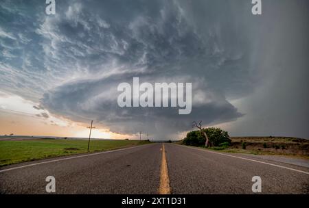 Ein dramatischer Superzellensturm mit einer wirbelnden Wolkenbildung erhebt sich über einer leeren Autobahn, die sich in der Abenddämmerung in den Horizont zieht. Butler, Oklahoma United Stat Stockfoto