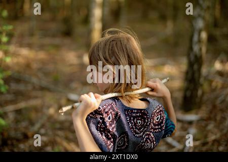 Ein Kind mit einem Holzstock über der Schulter steht inmitten eines Waldes und wirft einen nachdenklichen Blick in die Ferne. Bola02447 Copyright: XConnectxIma Stockfoto