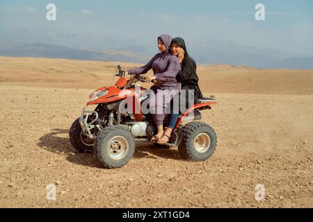 Zwei junge Mädchen lächeln, während sie auf einem roten Quad sitzen, in einer Wüstenlandschaft mit Bergen im Hintergrund. Bola02562 Copyright: XConnectxImagesx Stockfoto