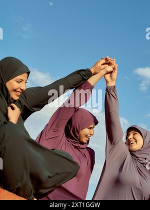 Drei Frauen in Hijabs halten die Hände in Solidarität unter blauem Himmel zusammen. Bola02596 Copyright: XConnectxImagesx Stockfoto