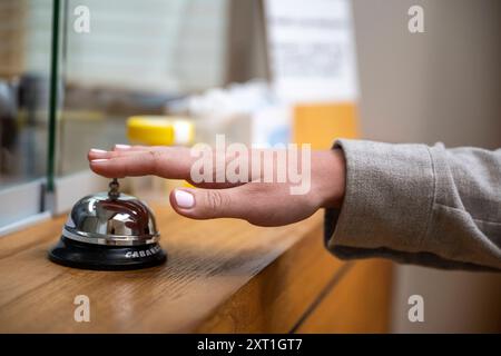 Wachttijden in de zorg Eine Nahaufnahme der gestreckten Hand einer Person, die eine Serviceklingel auf einem Holztheken drückt. Molenhoek Nederland DEL 20240606 Stockfoto