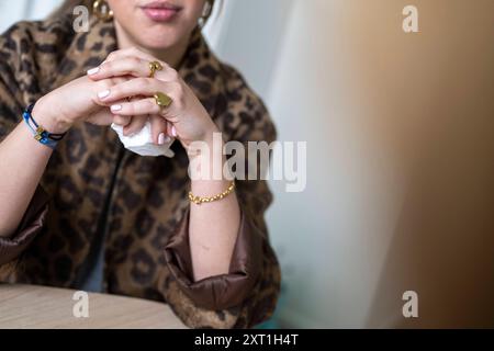 In der Nahaufnahme der Hände einer Frau, die elegant auf einem Tisch liegt, in einer Bluse mit Leopardenmuster und einem stilvollen Schmuckstück Stockfoto