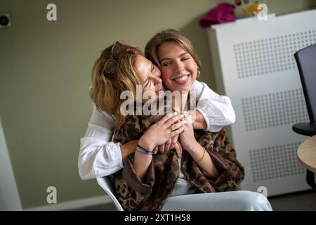 Unterschiedliche Situationen in een huisartsenpraktijk zwei Frauen teilen sich eine fröhliche Umarmung, wobei eine ihren Kopf auf der anderen Schulter legt, beide lächeln warm in einem i Stockfoto