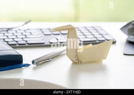 Ein Papierboot aus gefaltetem Blatt mit gedrucktem Text sitzt auf einer weißen Oberfläche vor einem Hintergrund mit Tastatur und Stift auf einem Notebook. Stockfoto