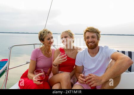 Drei Freunde genießen Drinks, während sie in der Abenddämmerung auf einem Segelboot entspannen. Stef00139 Copyright: XConnectxImagesx Stockfoto