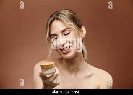 Eine junge Frau mit Vitiligo hält einen Cremebecher, lächelt und blickt hinunter. Stockfoto