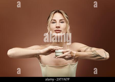 Eine junge Frau mit Vitiligo hält ein Cremeglas vor sich und blickt direkt in die Kamera. Stockfoto