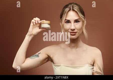 Eine junge Frau mit Vitiligo hält ein Glas Creme und zeigt ihr Selbstvertrauen und Engagement für die Hautpflege. Stockfoto