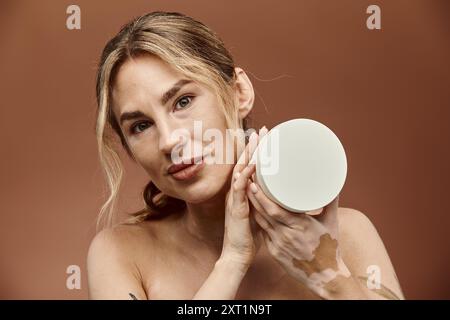 Eine junge Frau mit Vitiligo hält einen weißen Cremebehälter vor ihr Gesicht. Stockfoto