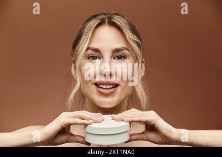 Eine junge Frau mit Vitiligo lächelt und hält auf beigefarbenem Hintergrund ein Sahneglas vor sich. Stockfoto