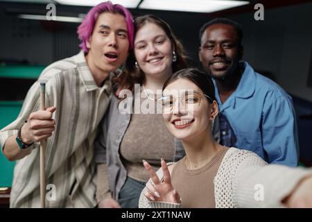 Eine Gruppe von Freunden genießt gemeinsame Zeit in der Poolhalle und macht Selfie mit fröhlichen Ausdrücken. Sichtbare Billardtische und Hinweise im Hintergrund schaffen eine entspannte Atmosphäre Stockfoto